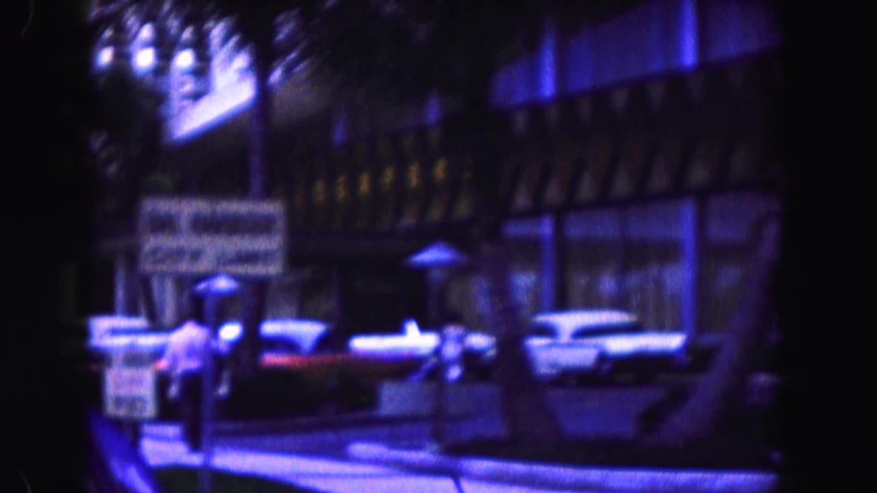 Parked classic cars outside a hotel frontage with sidewalk signs and a pedestrian nearby.
