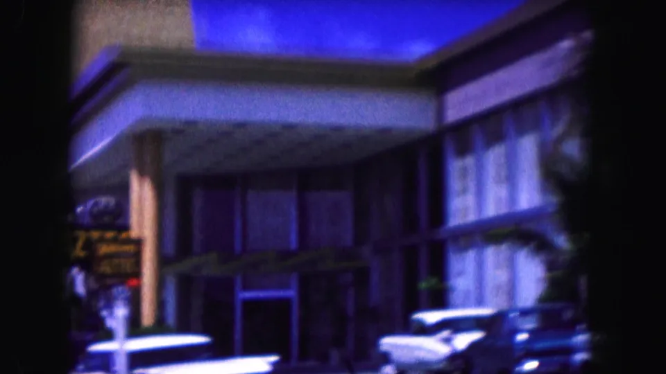 1960 Miami street view from 8mm footage showing a commercial facade, parked classic cars, and dark film-edge framing.