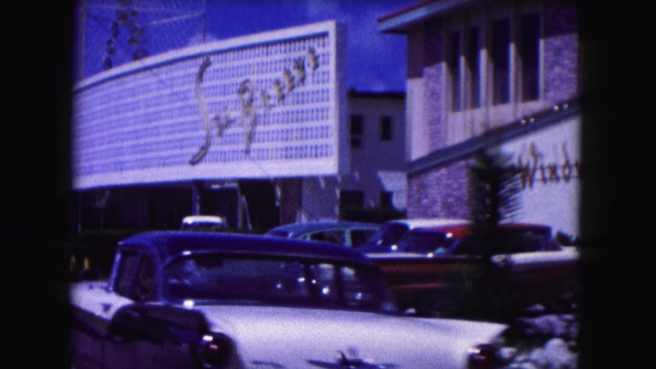 Large building sign above parked classic cars on a sunny street.