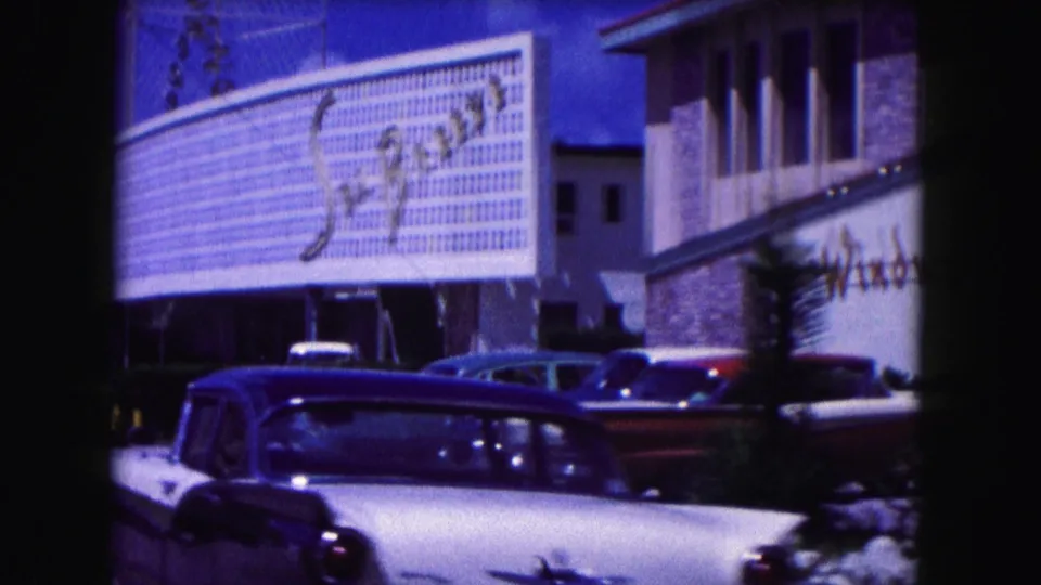 1960 Miami footage appears to show a large signed facade with classic cars parked along the curb under bright blue sky.