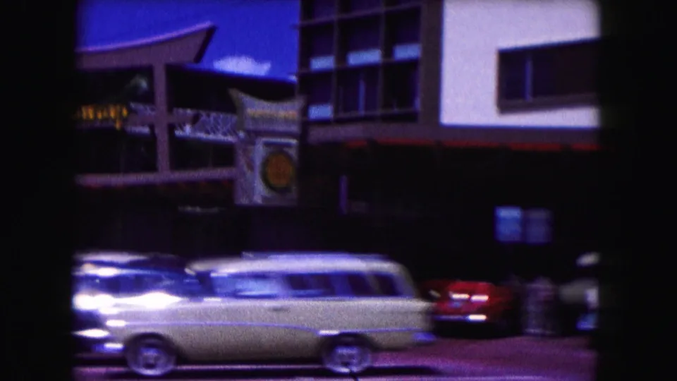 1960 Miami street view with a signed commercial building, awning details, and mid-century cars moving past the storefront.