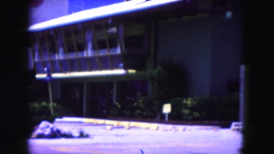 1960 Miami street view from 8mm footage, showing a modern building, roadway, parked cars, and heavy film-frame obstruction.