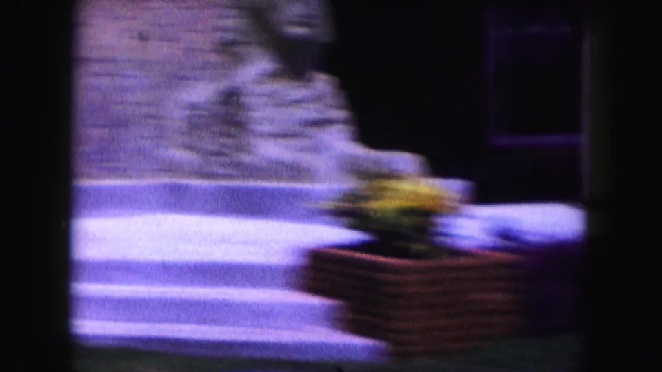 1960 Miami 8mm frame with motion blur across a roadside statue, brick planter, and passing vehicle.