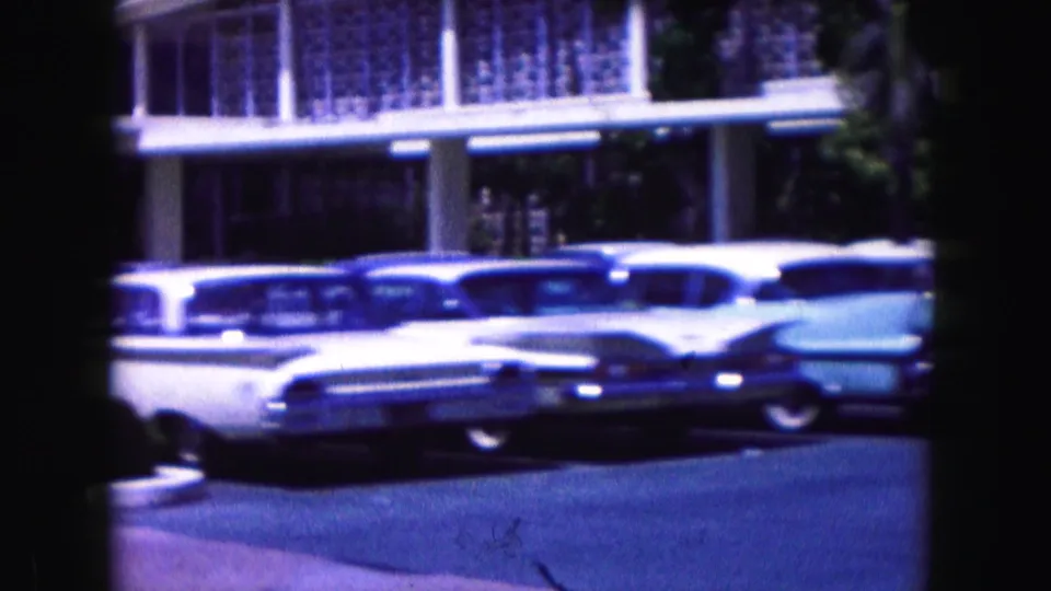 1960 Miami 8mm frame showing tailfin-era cars parked beside a modernist building with windows and columns.