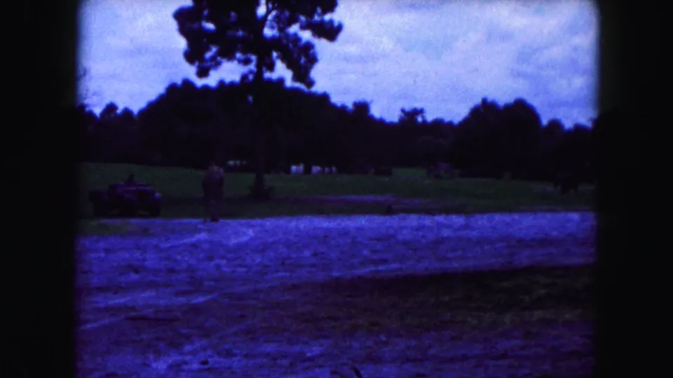 1960 Miami-area 8mm frame with a small vehicle near a grassy animal enclosure, trees, and a cloudy sky.