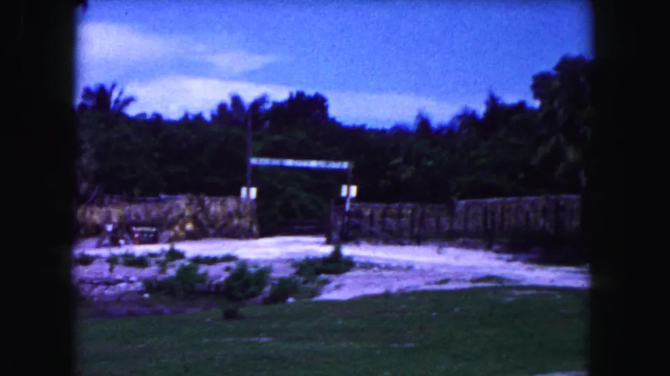 1960 Miami home-movie view of a landscaped park enclosure with stone wall, palms, open grass, and a distant archway.