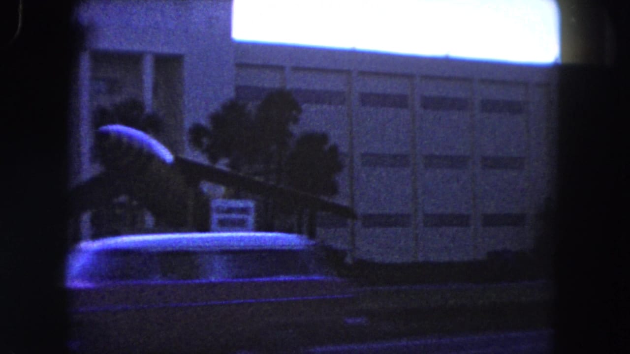 Aircraft display outside a modern building with palm trees and a passing car.