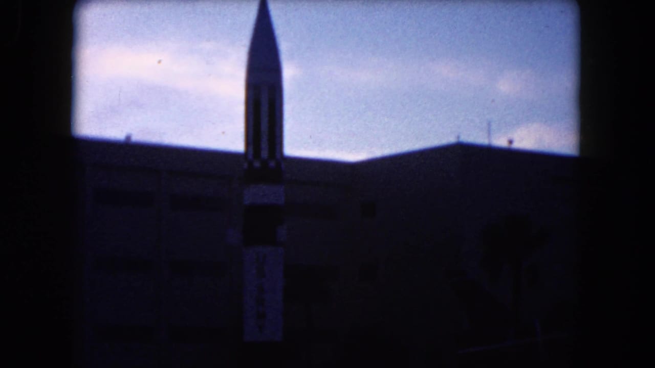 Rocket-shaped display silhouetted against sky near a modern building.