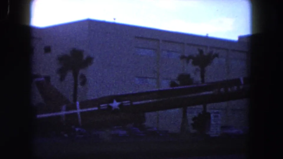 1960 Miami view of an aircraft display with a visible military star marking, set before palm trees and a modern building facade.