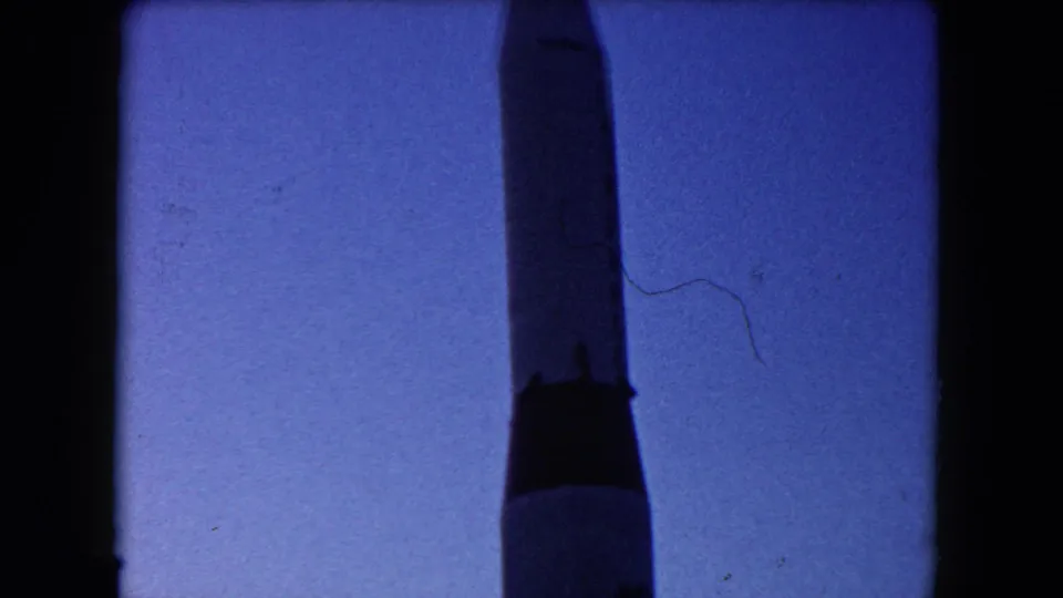 Nearly full-height view of the rocket replica in the supplied 1960 Miami footage, with blue-shifted sky and visible film wear.