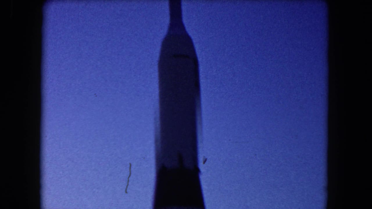 1960 Miami 8mm frame showing a tall rocket-like silhouette against a deep blue dusk sky.