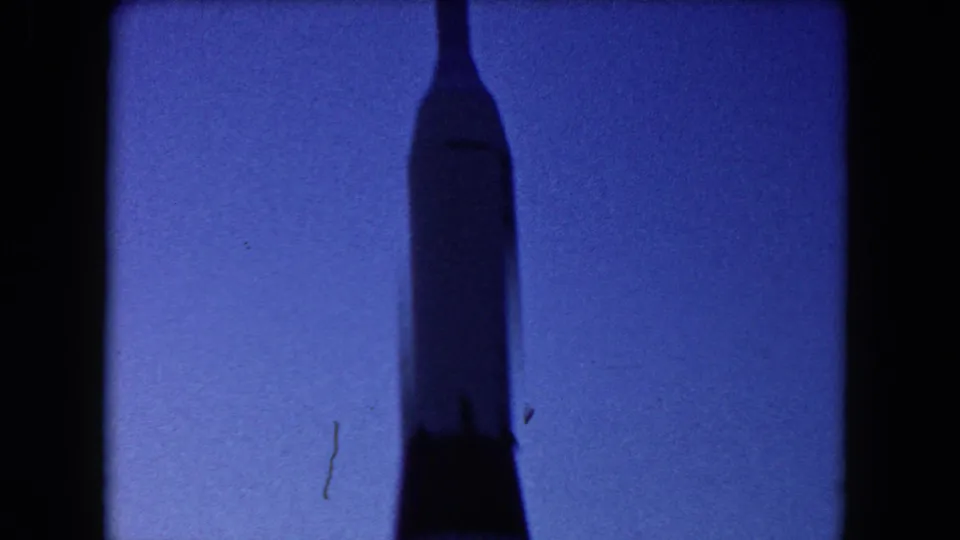 1960 Miami 8mm frame showing a tall rocket-like silhouette against a deep blue dusk sky.