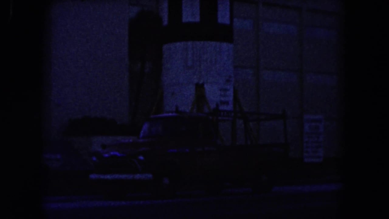 Dim 1960 Miami street scene with a work truck parked near a tall structure and partially visible signage.