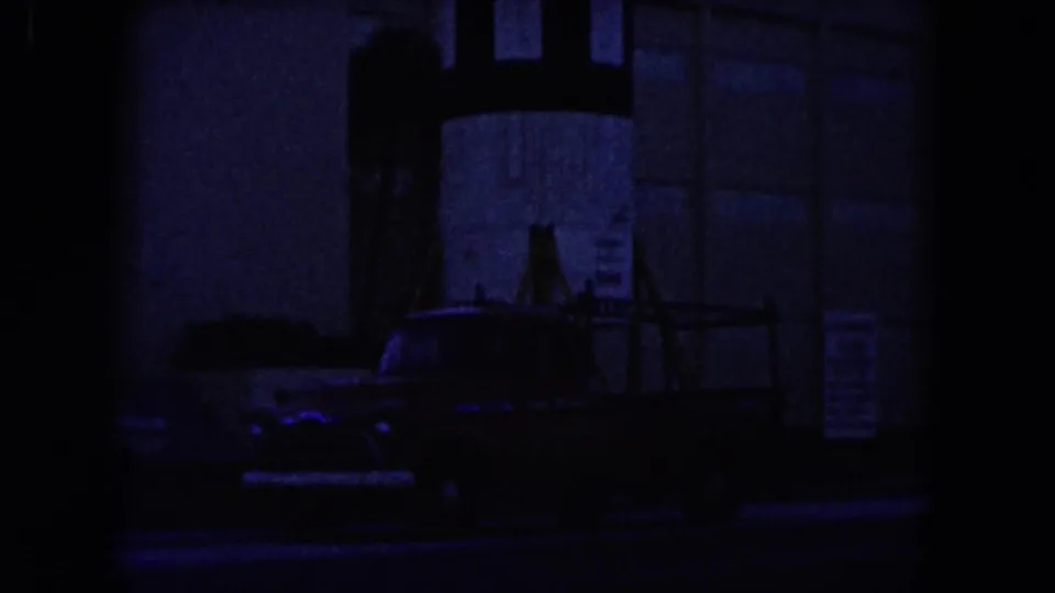 Dim 1960 Miami street scene with a work truck parked near a tall structure and partially visible signage.