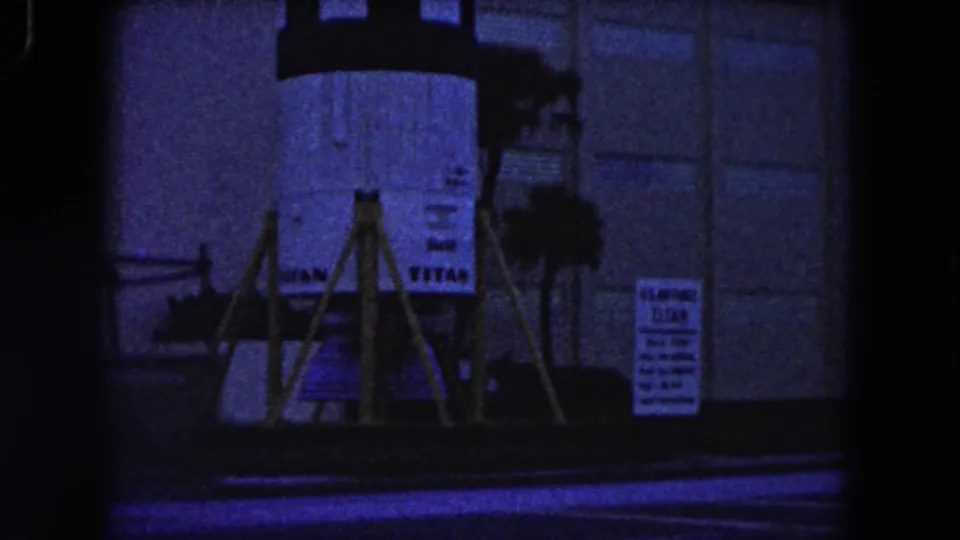 1960 Miami 8mm frame showing a supported rocket-like structure with signs and people near its base.