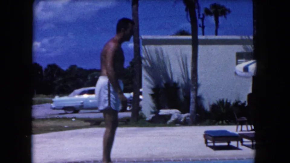 At the end of the Miami poolside clip, the shirtless man stands near lounge chairs, a white building, palms, and a vintage car.