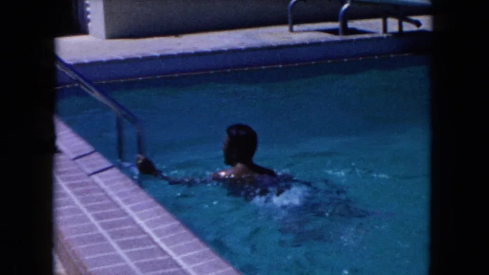 1960 Miami pool footage showing a swimmer in blue water near a metal handrail, with tile edging and the pool deck in view.