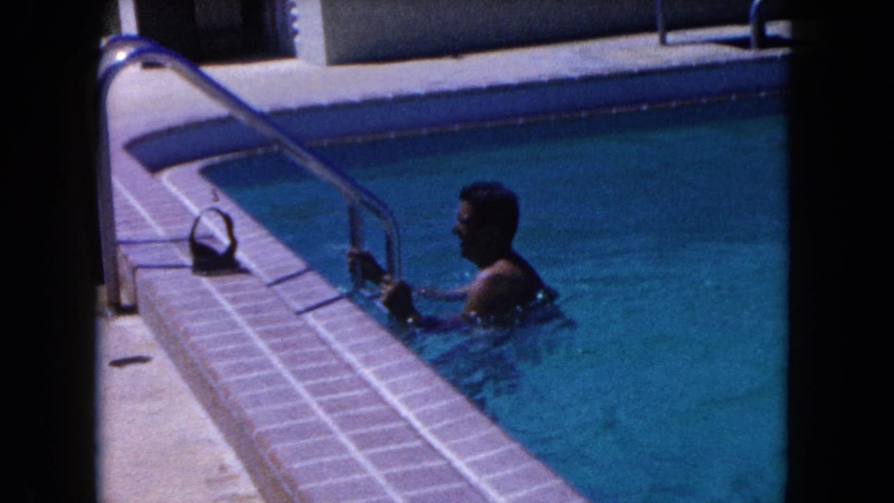 Man in pool water faces the ladder beside the tiled pool edge.