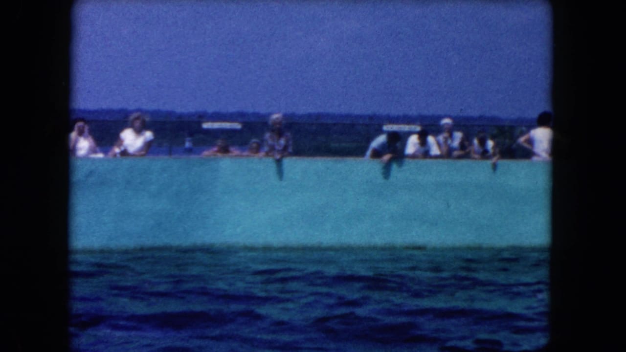 People line a turquoise wall while dark blue water fills the foreground.
