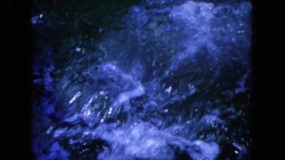 A burst of splash and bubbles fills the frame as the dolphin moves below or at the water surface in faded 8mm footage.