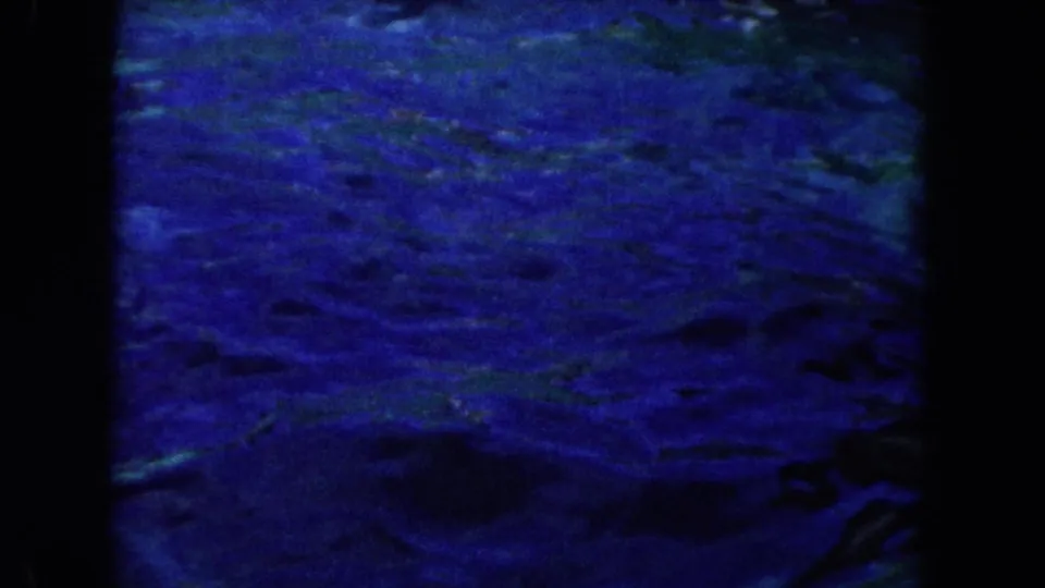 1960s Miami-area 8mm frame showing dark blue water in a contained aquatic setting, with heavy grain and black film edges.