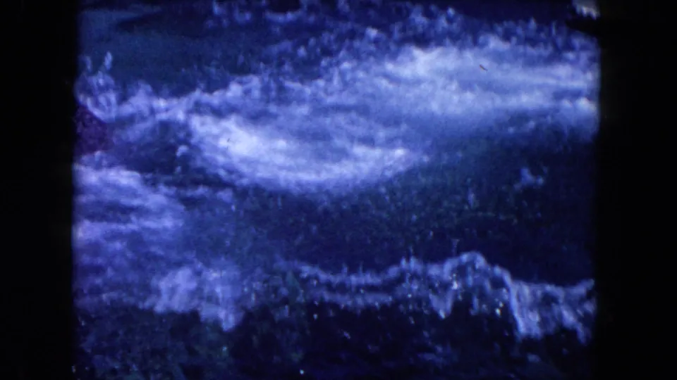 1960 Miami frame showing foamy water and a blurred dolphin form moving through the pool after a jump or turn.