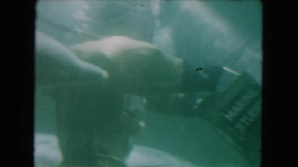 1960 Miami underwater 8mm frame showing a diver reaching near marine animal forms and a Marine Studios-labeled container.