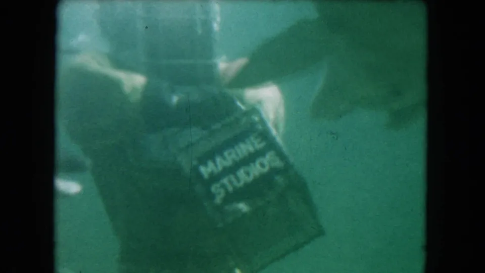 1960 Miami underwater frame showing a Marine Studios-labeled box held near a dolphin and diving gear.