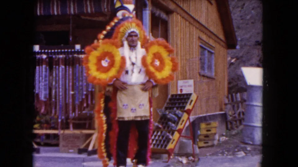 1960 Miami 8mm still of a costumed man posing with bright circular floral props near a storefront merchandise display.