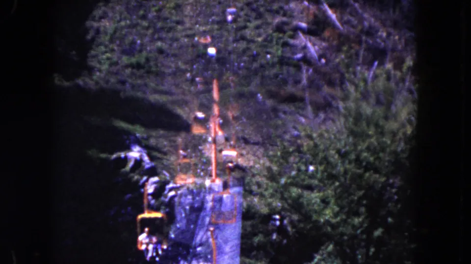 1960 Miami home-movie frame showing the tram route from farther back, with cable supports, a red chair, and dense hillside vegetation.