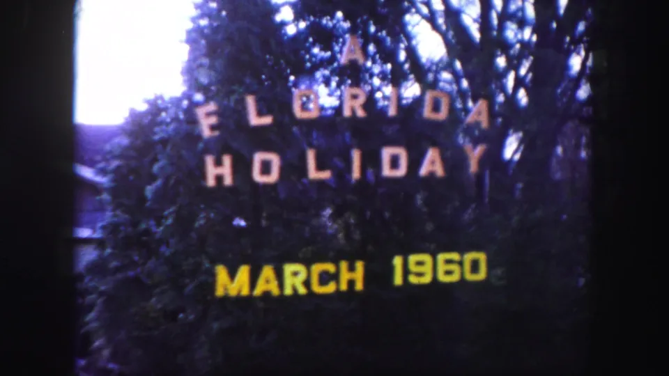 Vintage 8mm title frame for a 1960 Florida holiday film, with trees behind white and yellow lettering.