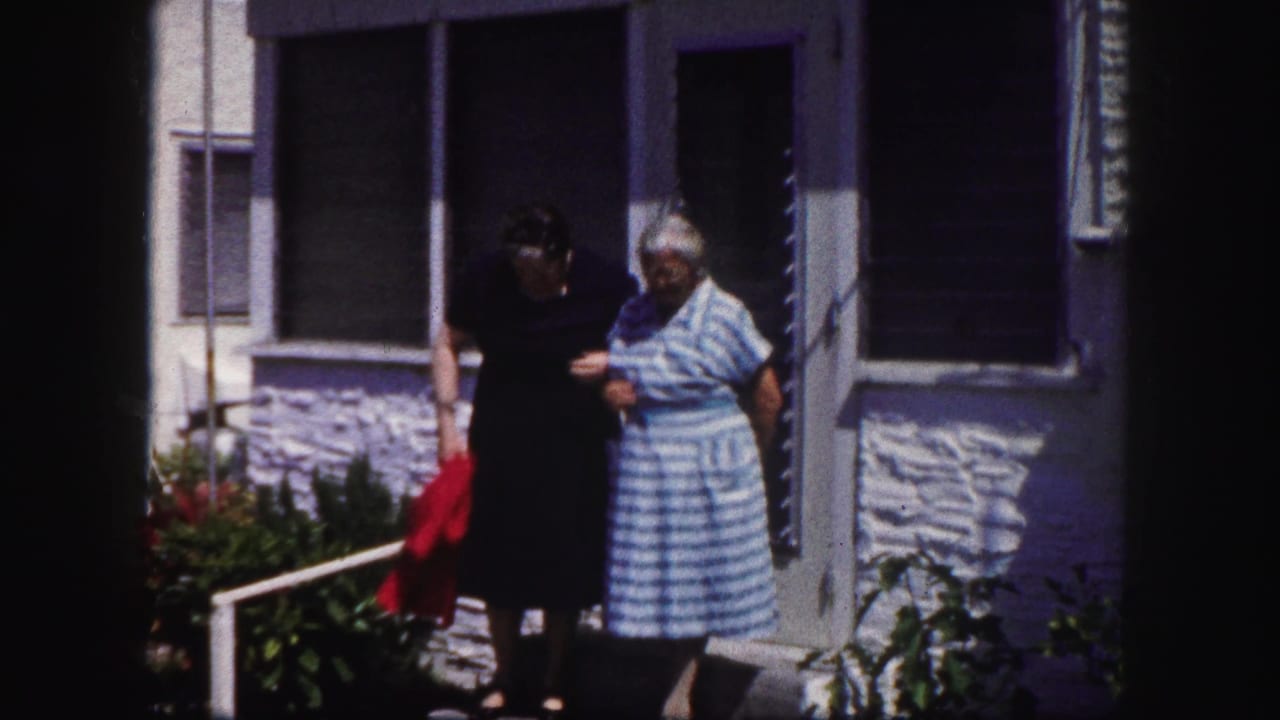 In 1960 Tampa home-movie footage, two adult women walk together by porch steps outside a residential house.