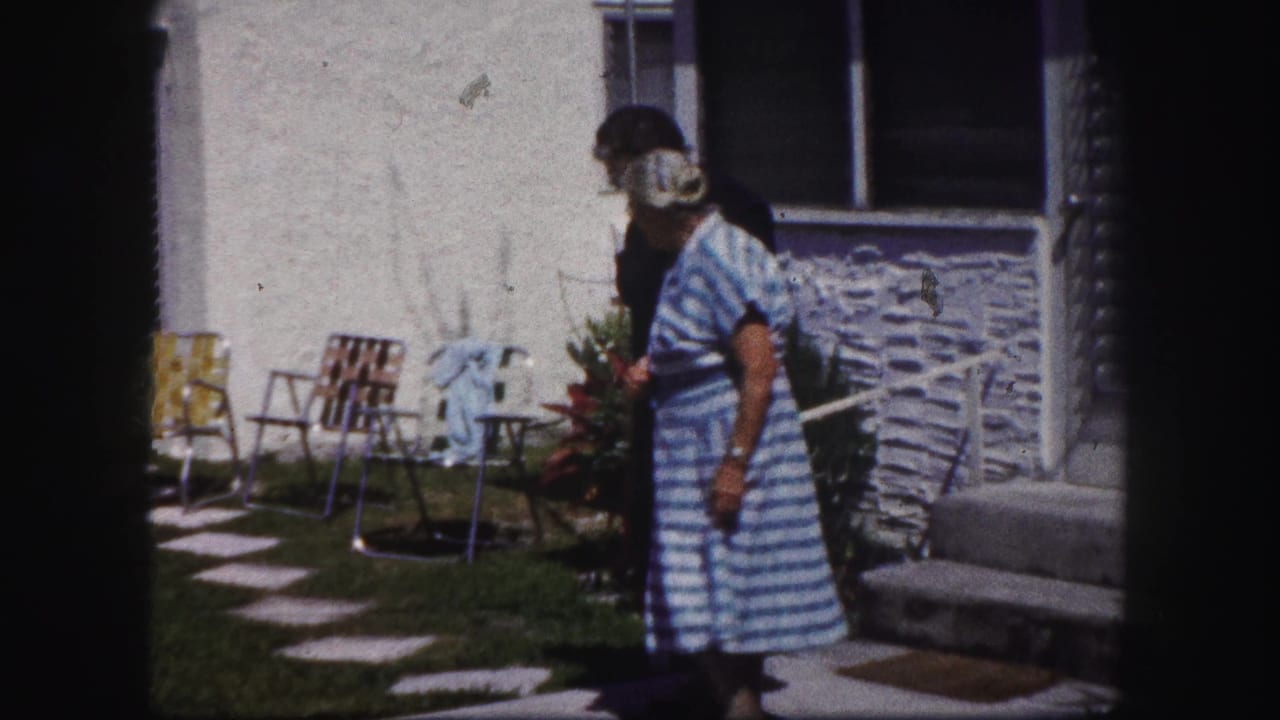 In 1960 Tampa home-movie footage, an older woman in a blue striped dress stands near a younger woman outside a house.