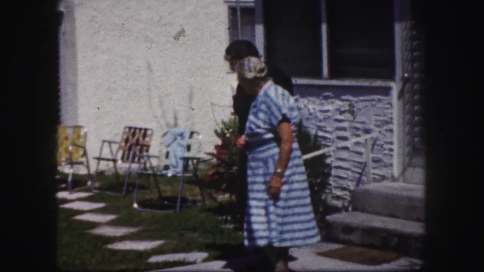 In 1960 Tampa home-movie footage, an older woman in a blue striped dress stands near a younger woman outside a house.