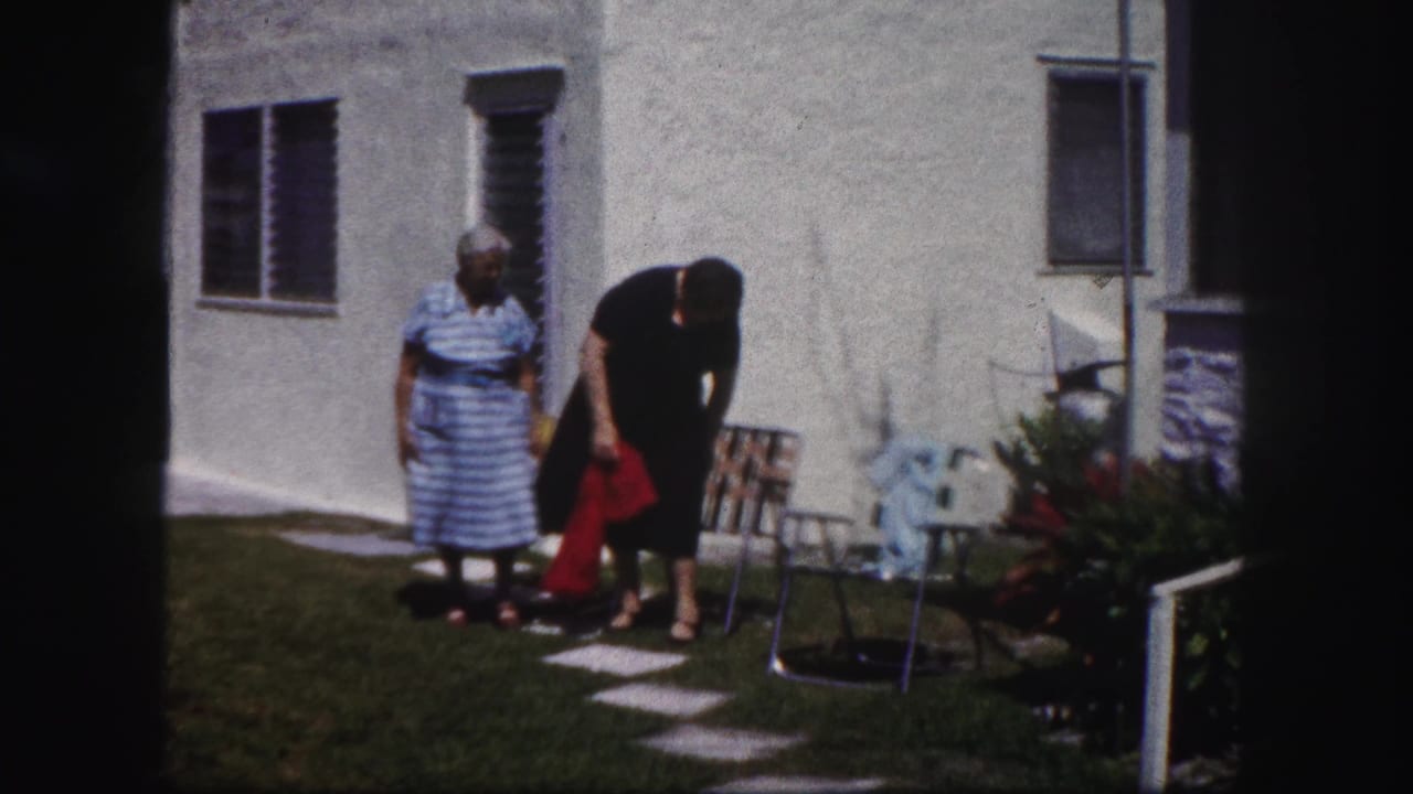 Two older women stand near lawn chairs outside a white stucco house.
