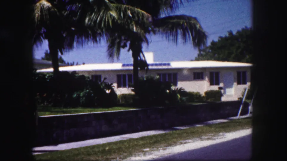 A white Tampa house with palms, shrubs, a low wall, and a bright sidewalk appears in 1960 home-movie footage.