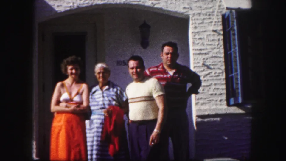 Four adults pose outside a white stucco house with an arched doorway in 1960 Tampa home-movie footage.