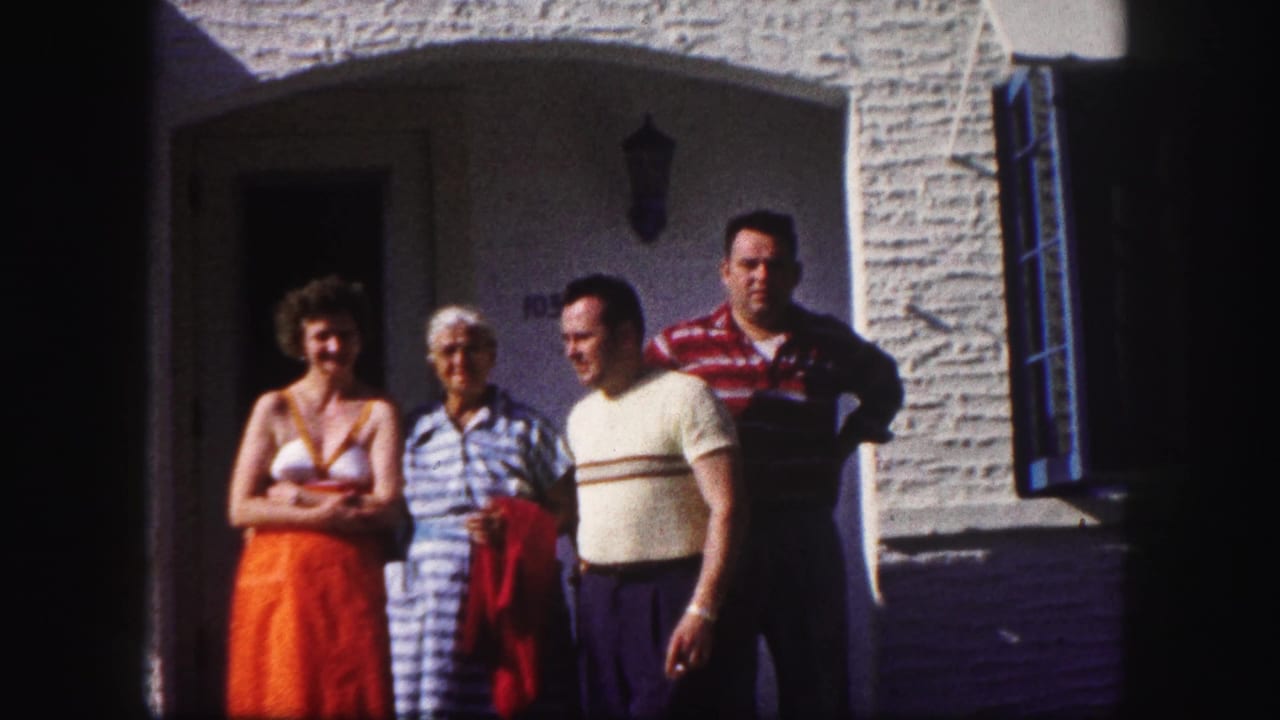 Four adults stand outside a white stucco house in bright sunlight.