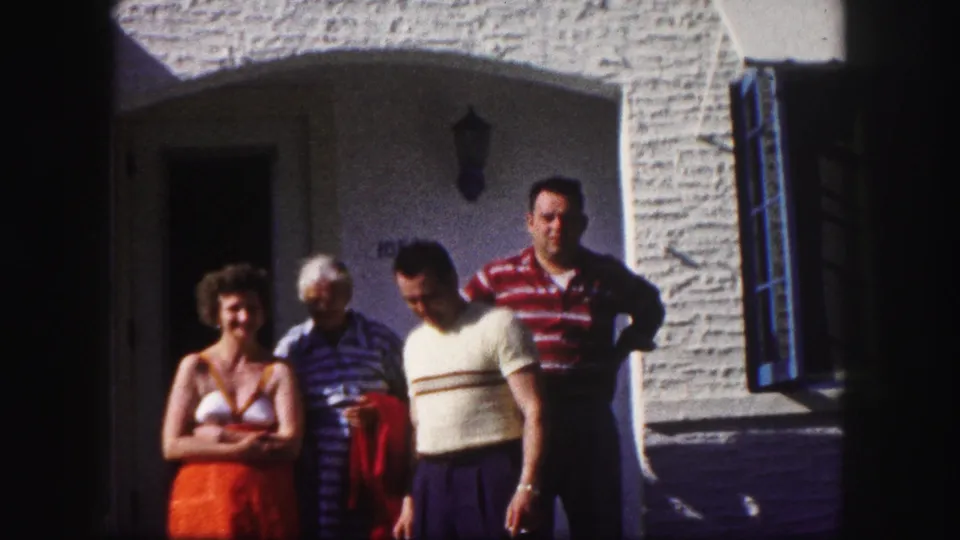 Four adults gather in front of the arched entry, with the woman in orange facing the camera and the men shifting position.