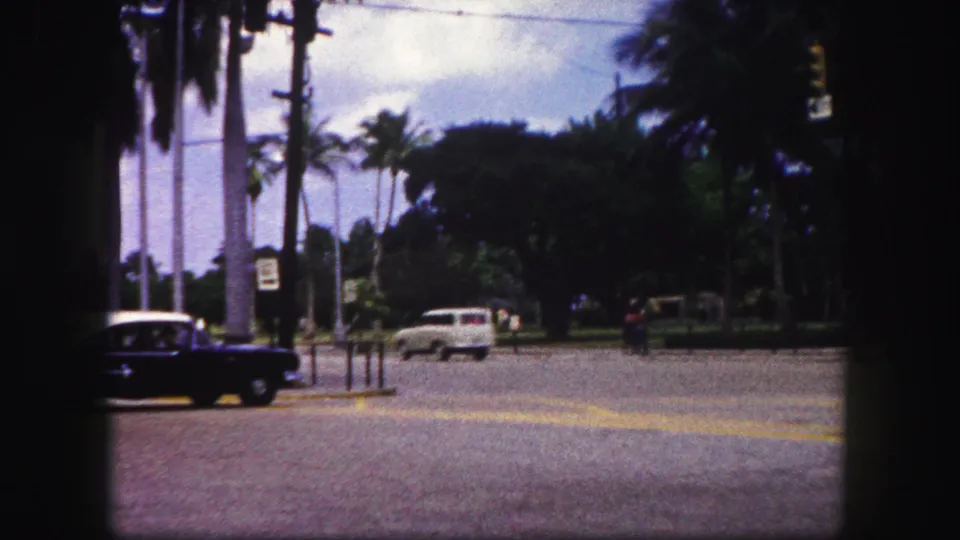 A white station wagon moves through the Tampa street scene as the dark sedan exits frame beside palms and traffic signs.