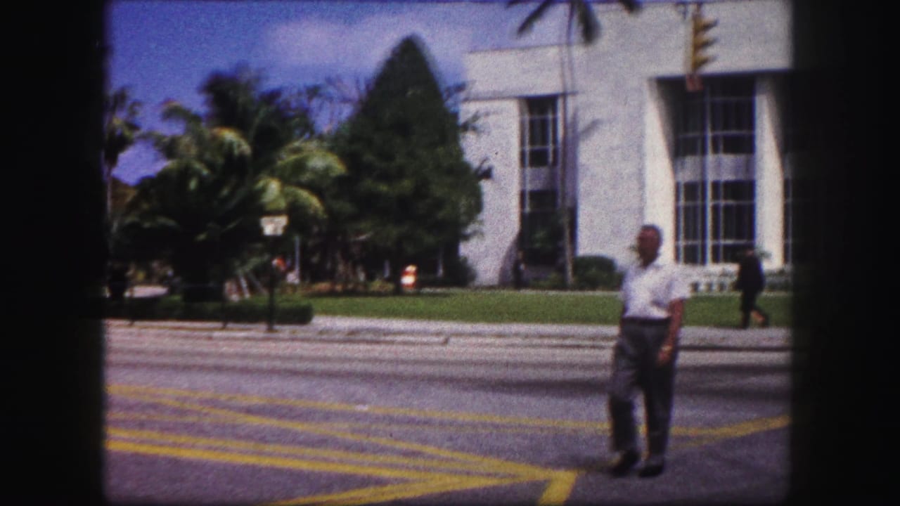 A man crosses the street in front of a white modernist-style building and palms in 1960 Tampa home-movie footage.