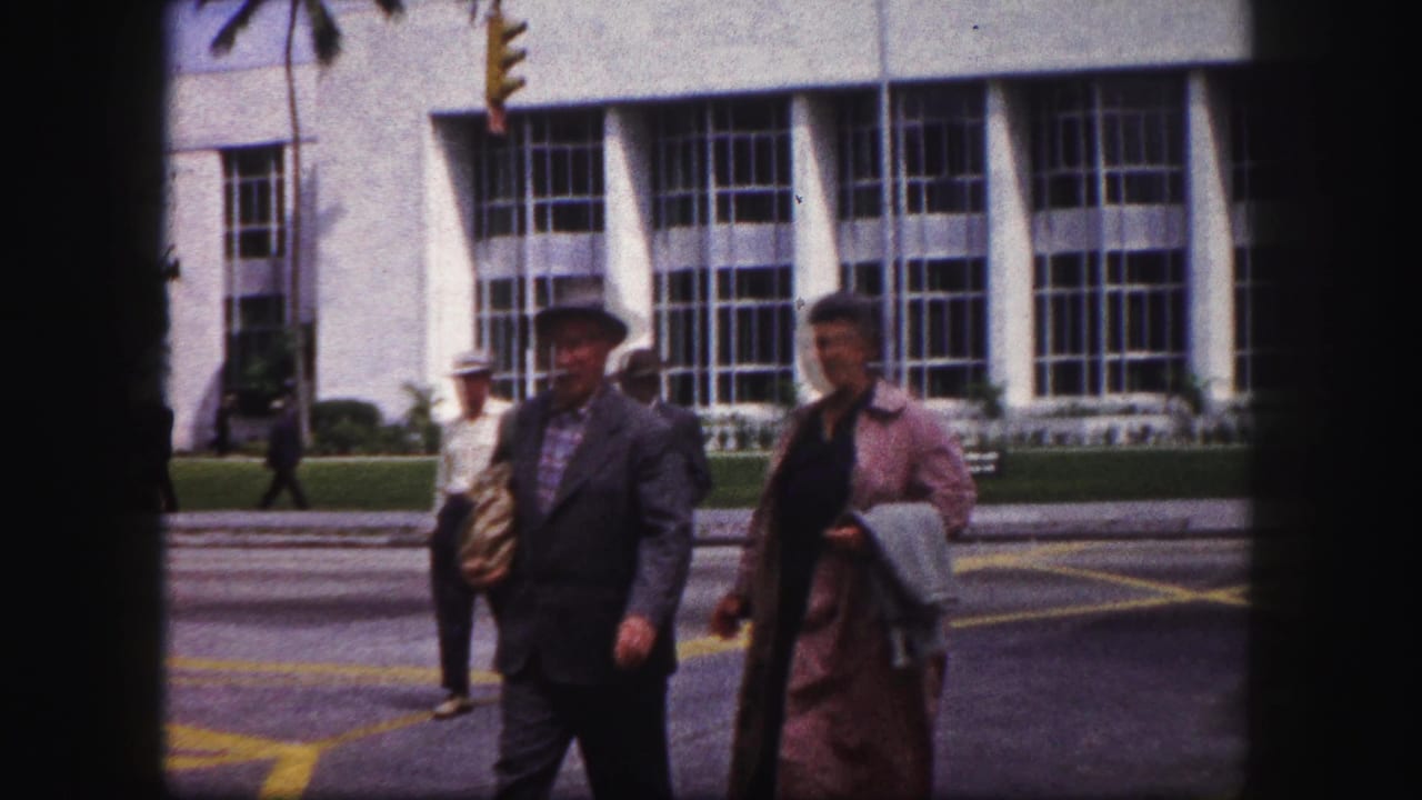 1960 Tampa pedestrians walk past the camera, with a traffic signal and large-window building visible behind them.