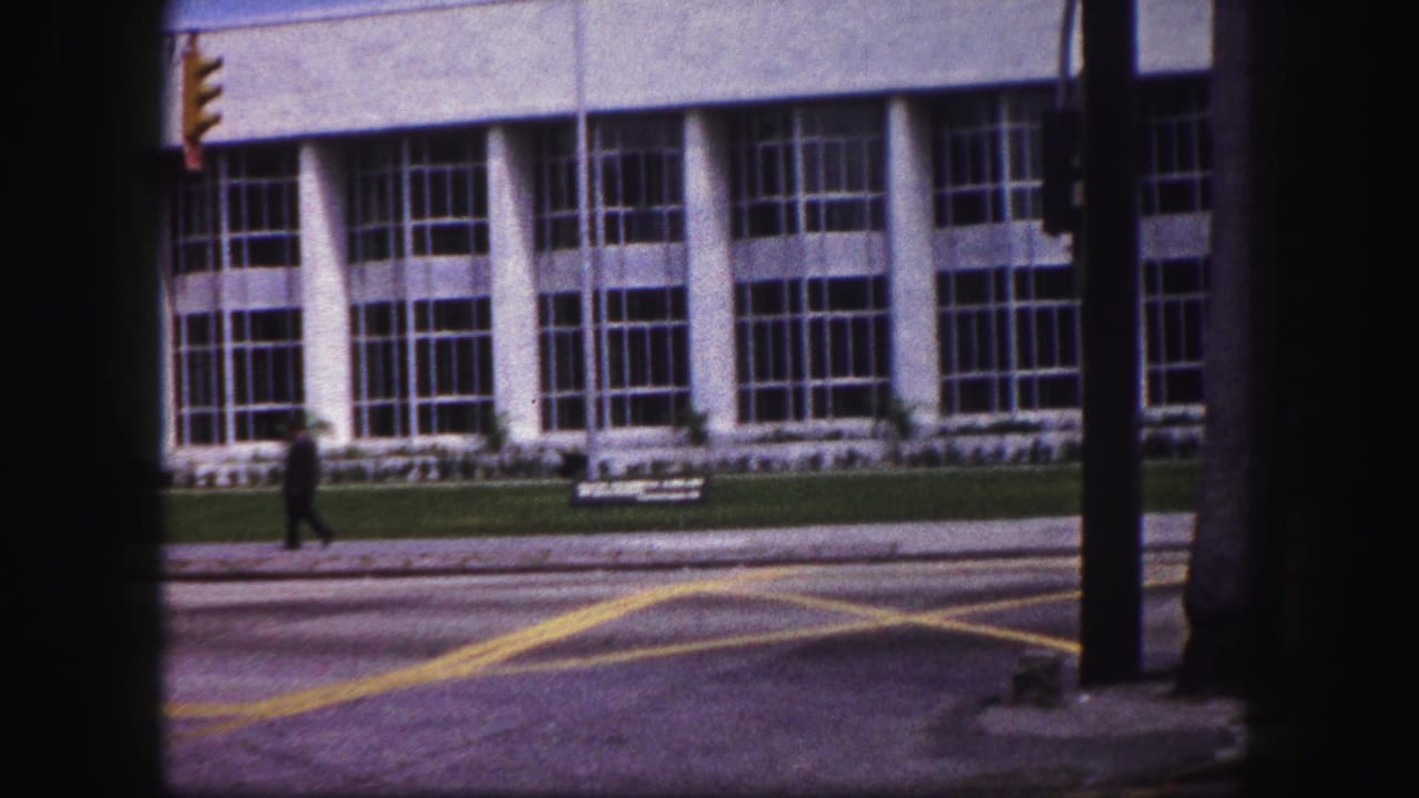 1960 Tampa street view with a distant walker, yellow road markings, a traffic light, and a large columned building.