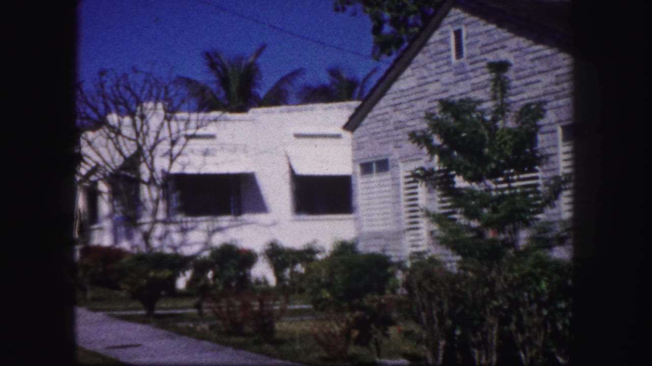 White stucco house with dark awnings beside a wood-sided structure and greenery.