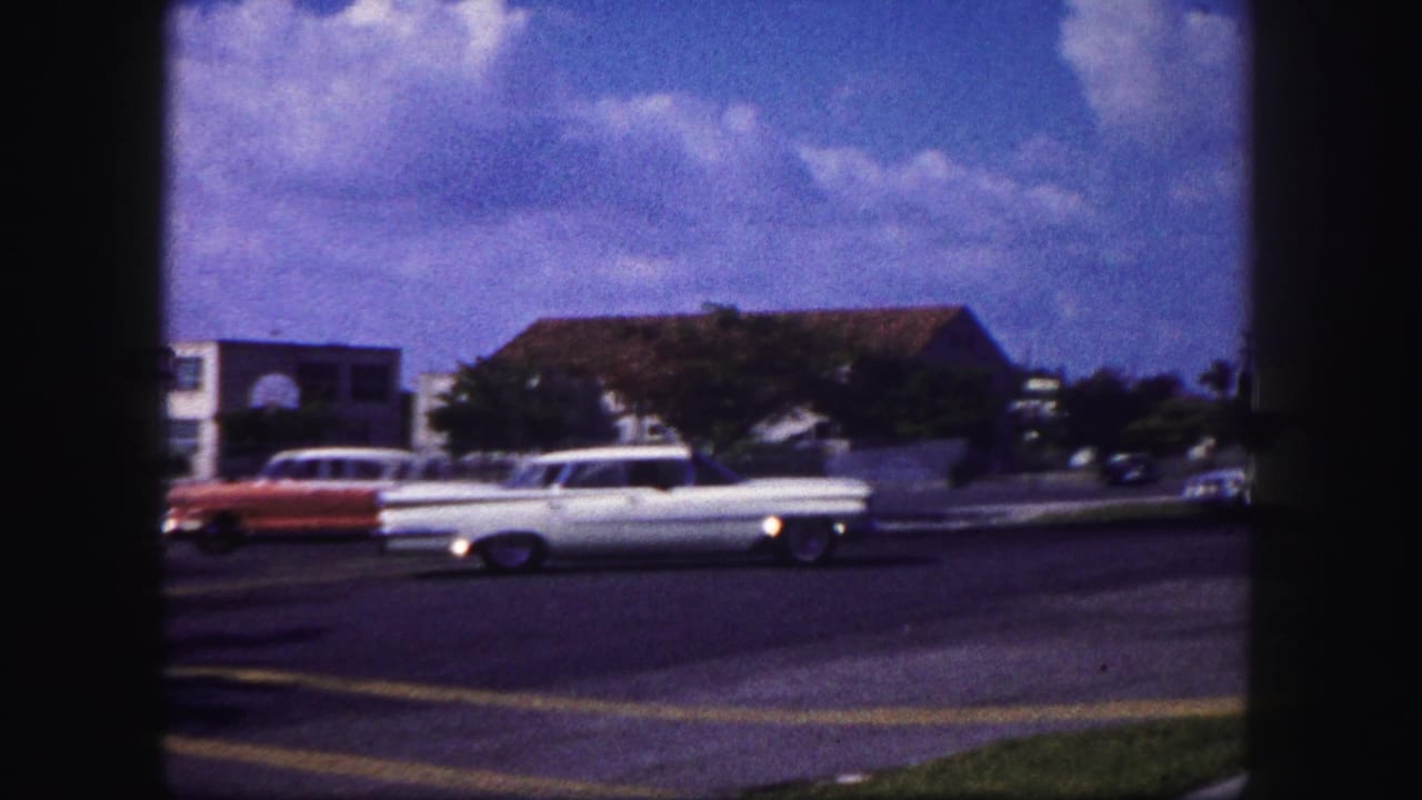White station wagon and red car on a sunny street near low buildings.