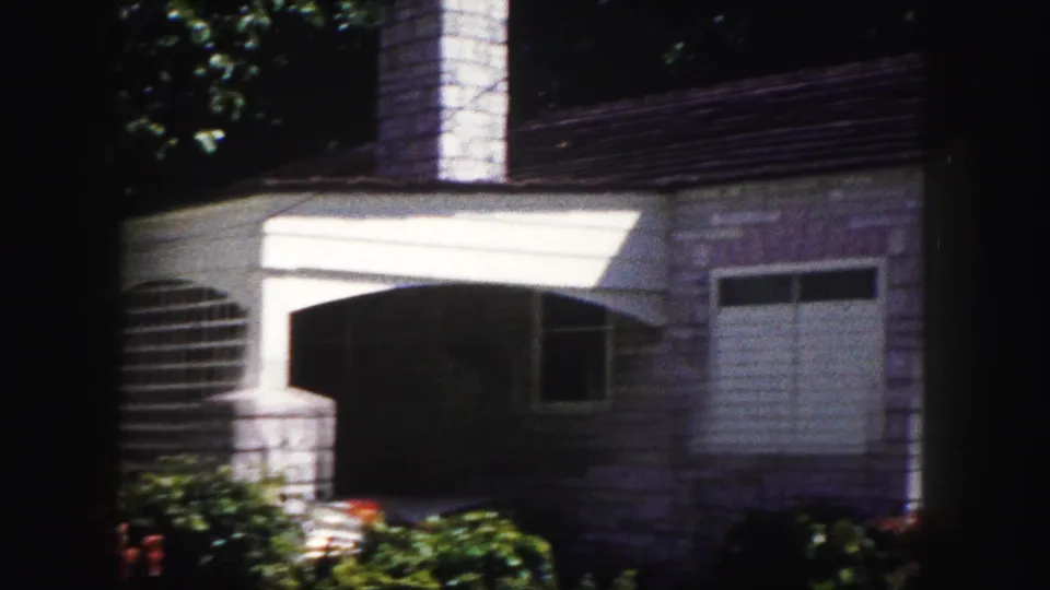 1960 Tampa house exterior with an arched garage opening, stone chimney, closed shutters, and planted landscaping.