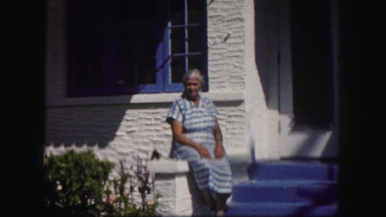 Woman in a blue striped dress seated on a white railing outside a stucco house.