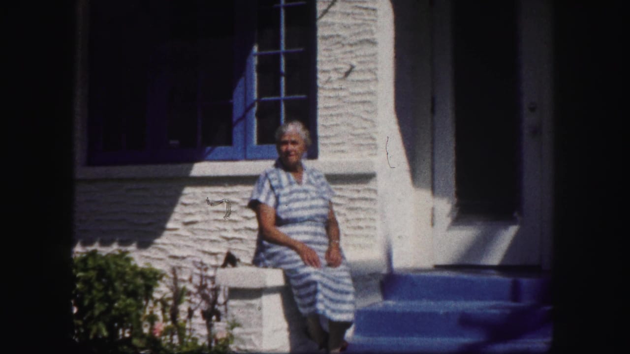 Woman seated beside a blue-framed window and white house entrance.