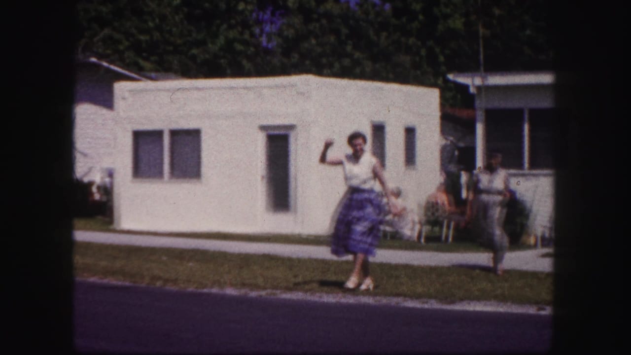 In 1960 Tampa home-movie footage, a woman waves toward the camera near a white mobile home as another woman stands farther back.