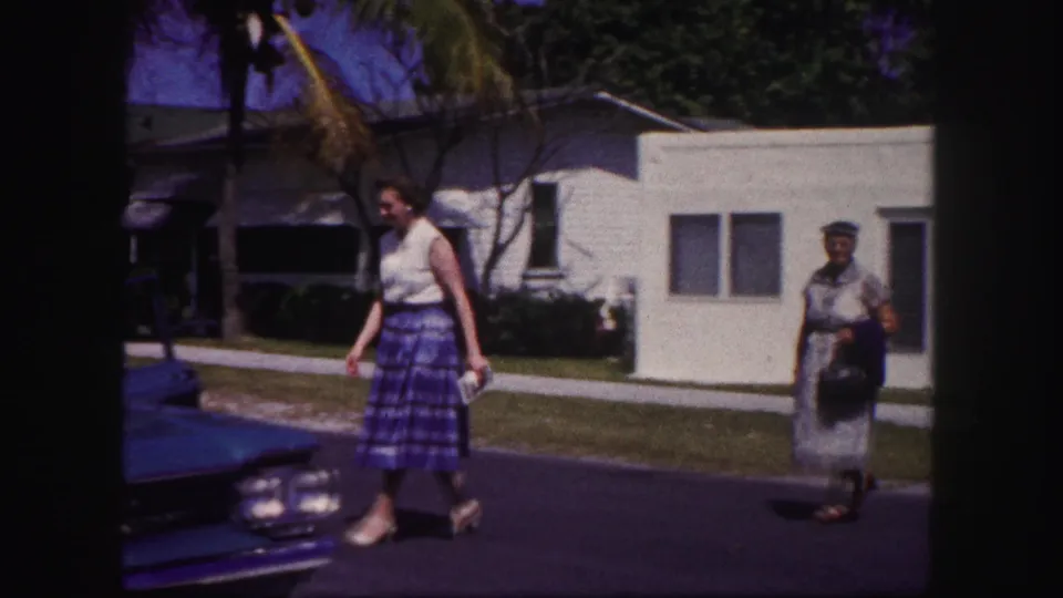 In the final frame, the woman passes a blue car at the edge of the street while another woman walks behind in the residential setting.
